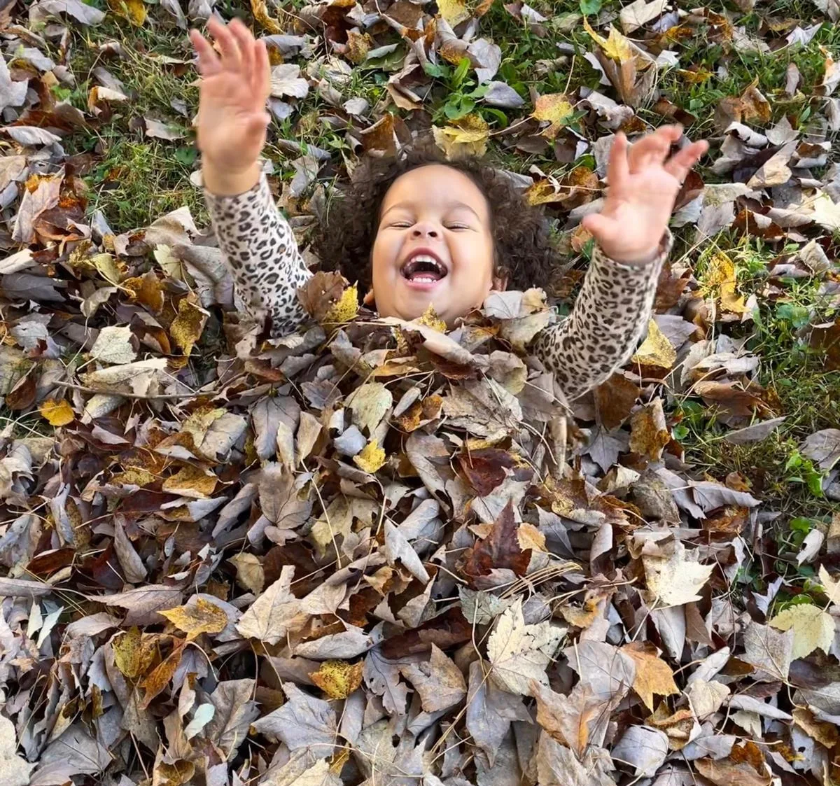 A child laughing in a pile of autumn leaves