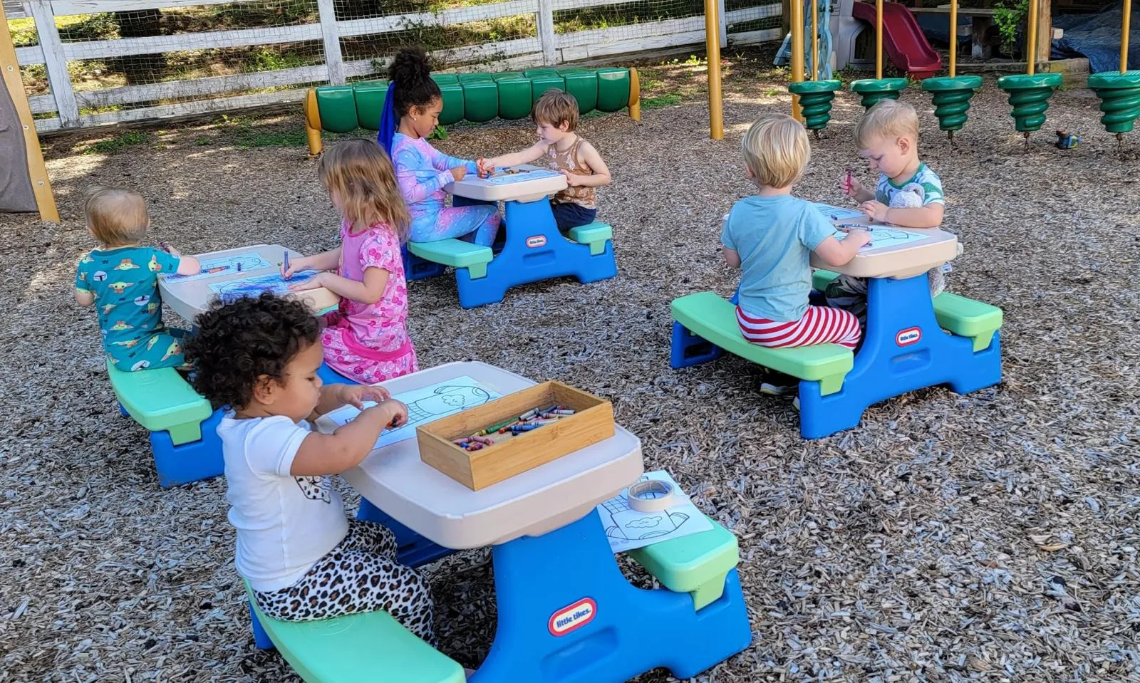 Children drawing at picnic tables out in the play yard