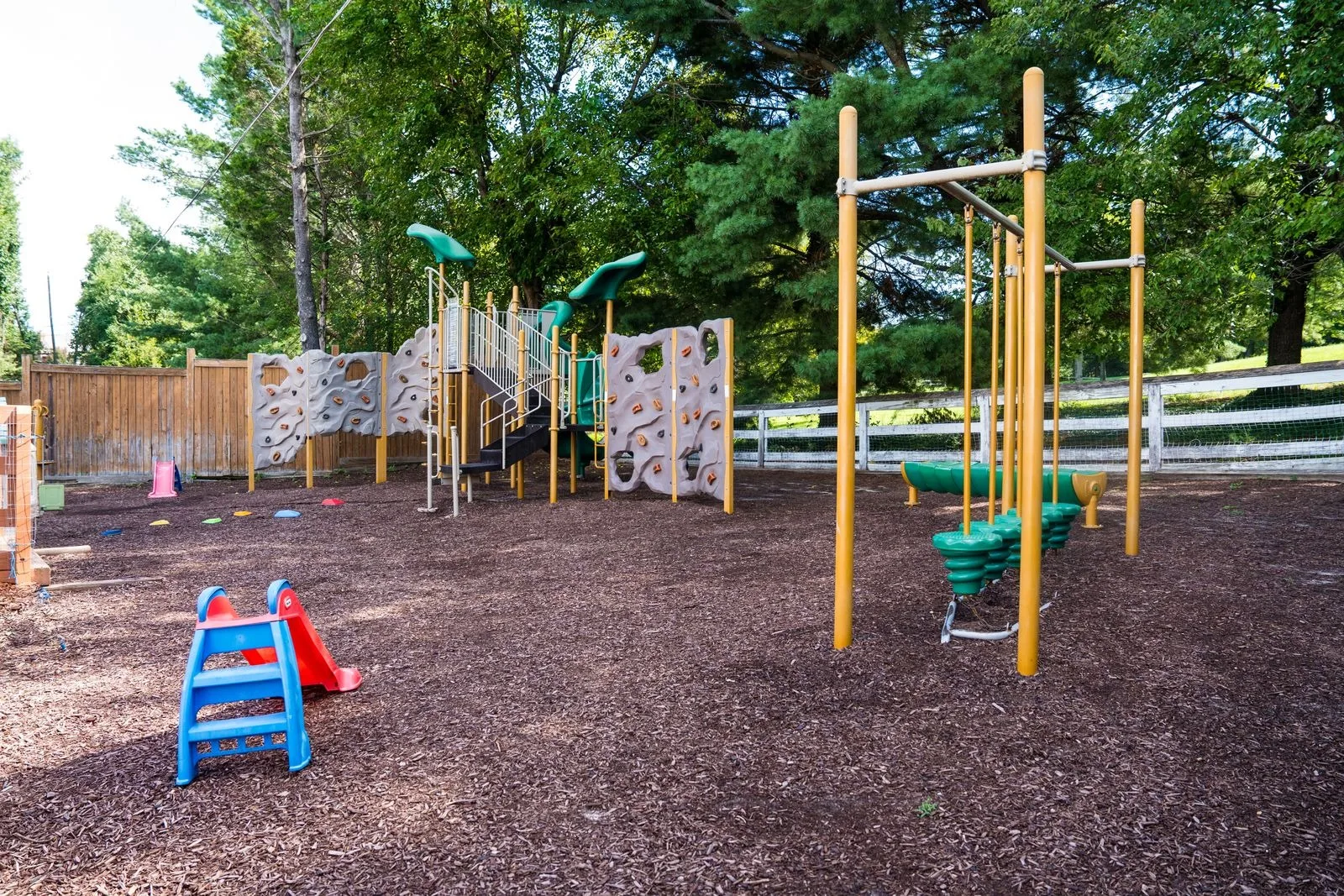 The mulched playground with a climbing structure, slide, and monkey bars