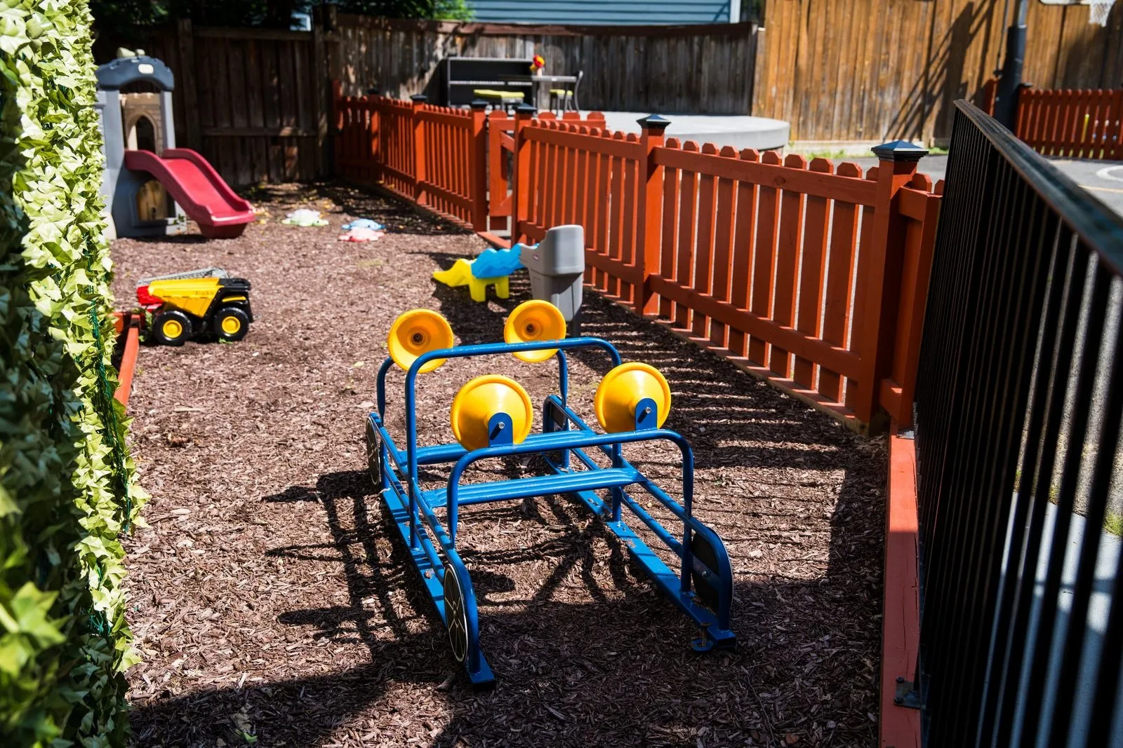 A four-seat glider in the fenced play area beside the toy trucks