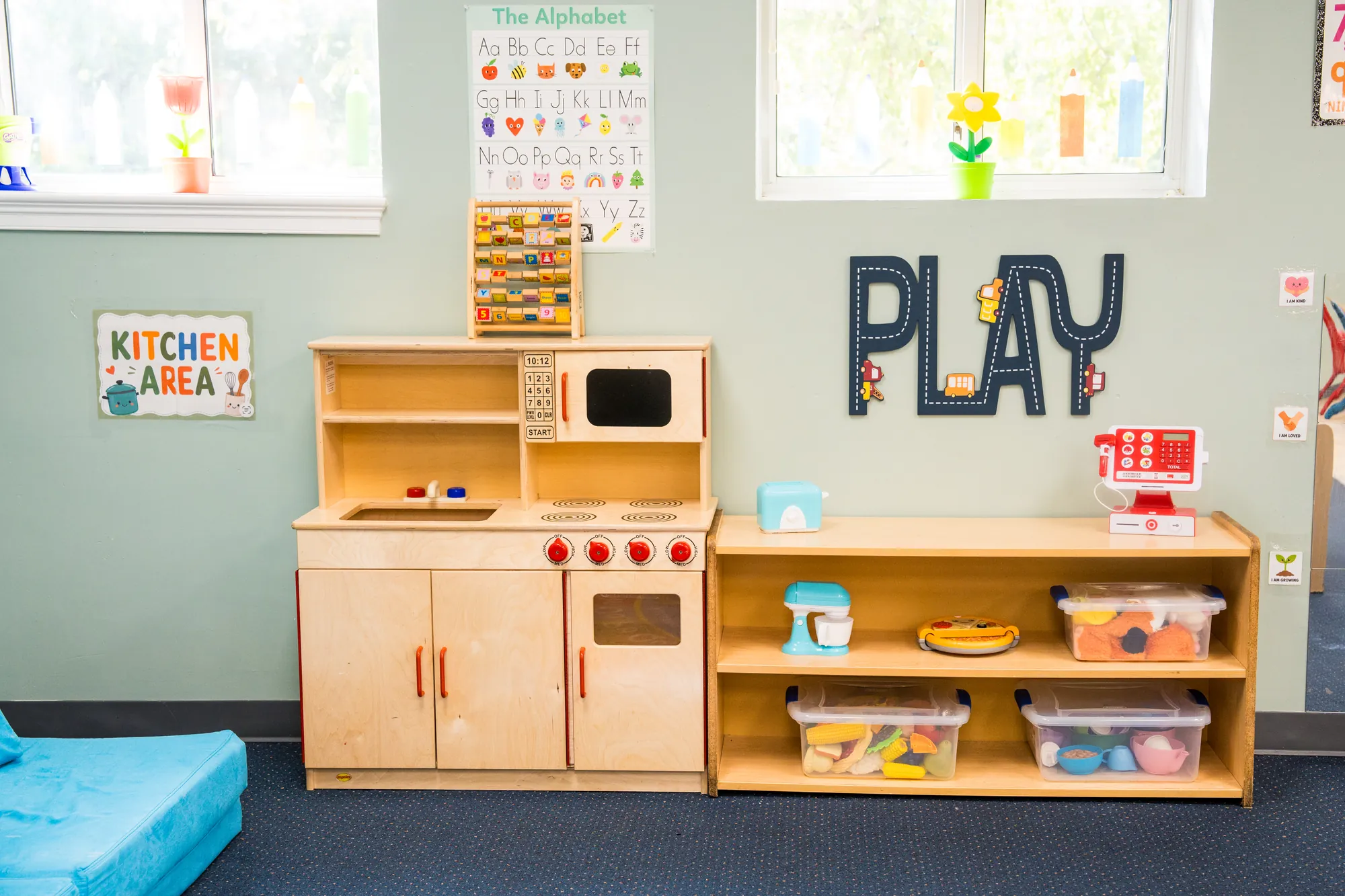 Toddler kitchen area with a wooden play kitchen under a PLAY wall sign