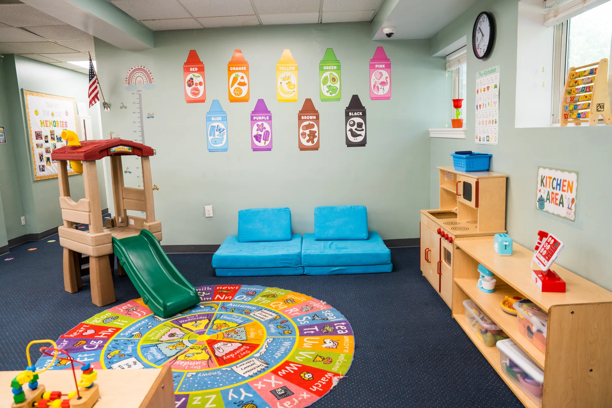 Toddler play area with a wooden playhouse, green slide, and calendar rug
